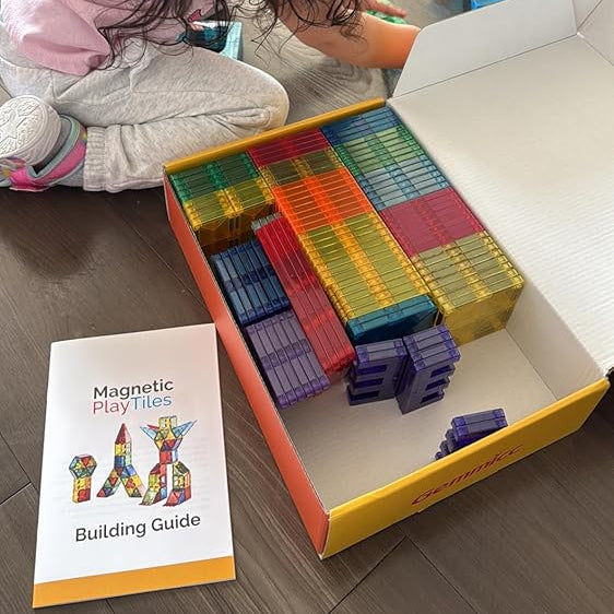 Child playing with colorful magnetic building toys on a wooden floor.