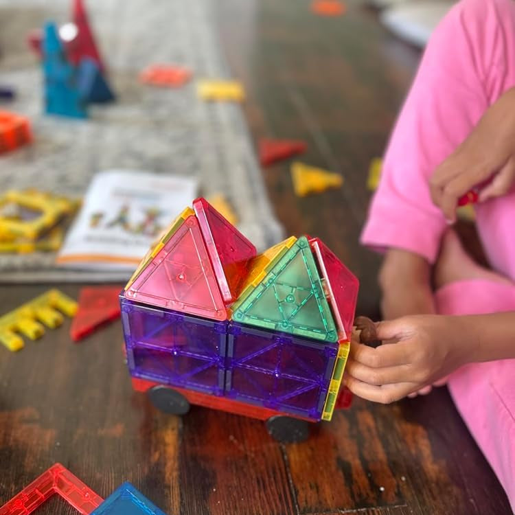 Colorful magnetic building blocks on a wooden table with a child's hand holding one block.